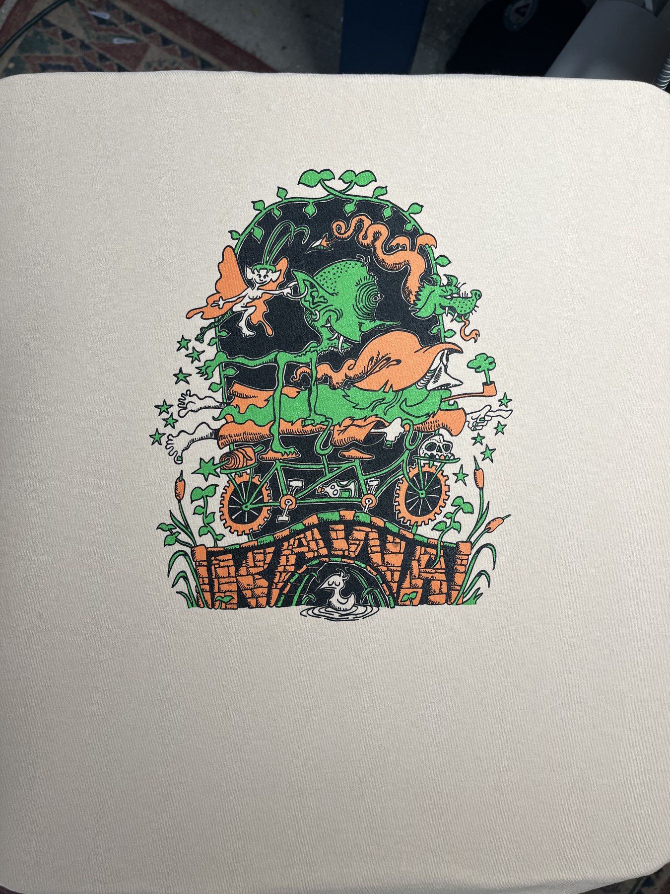 Green, orange, and black fantasy illustration screen printed on a light shirt
